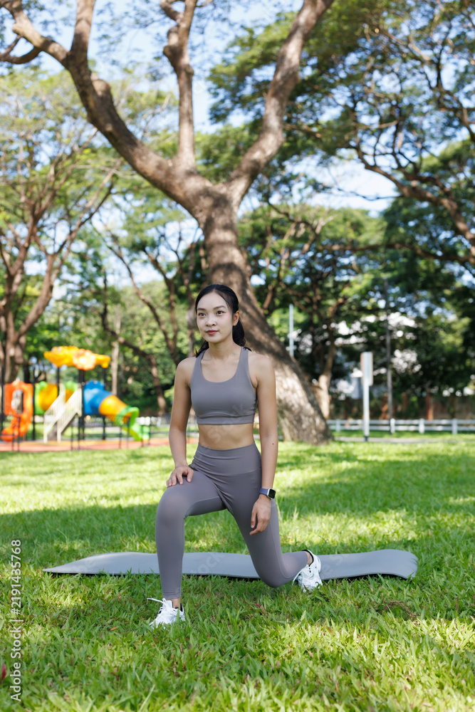 Obraz premium Young Asian woman performing lunges on a yoga mat in a green park, focusing on her outdoor fitness routine and practicing a healthy lifestyle for well-being