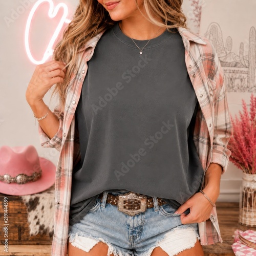 Cowgirl model in casual summer outfit. Western, southern woman in dark gray shirt with open plaid shirt over it, light blue frayed denim shorts. Howdy, country woman indoor mockup
