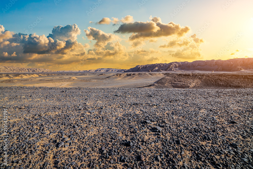 Obraz premium Vast arid desert landscape with rocky ground under golden sunset sky in Dahaidao, Xinjiang, China
