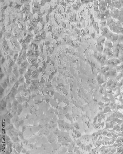 Close-up abstract texture of frosted glass block with translucent wavy patterns and distorted light, creating a soft architectural background.
