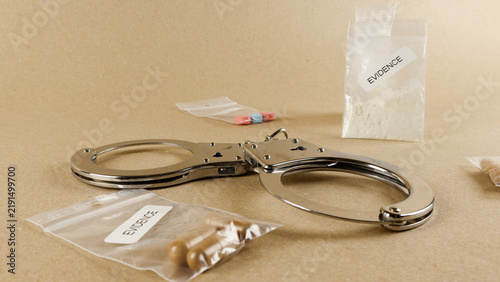 Konstfotografi Handcuffs beside multiple clear evidence bags of white powder, capsules and pill