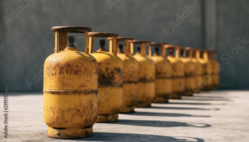 Row of aged yellow propane gas cylinders standing outdoors.