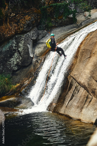 Fotografie Action shot of a canyoner rappelling down a cascading rocky waterfall