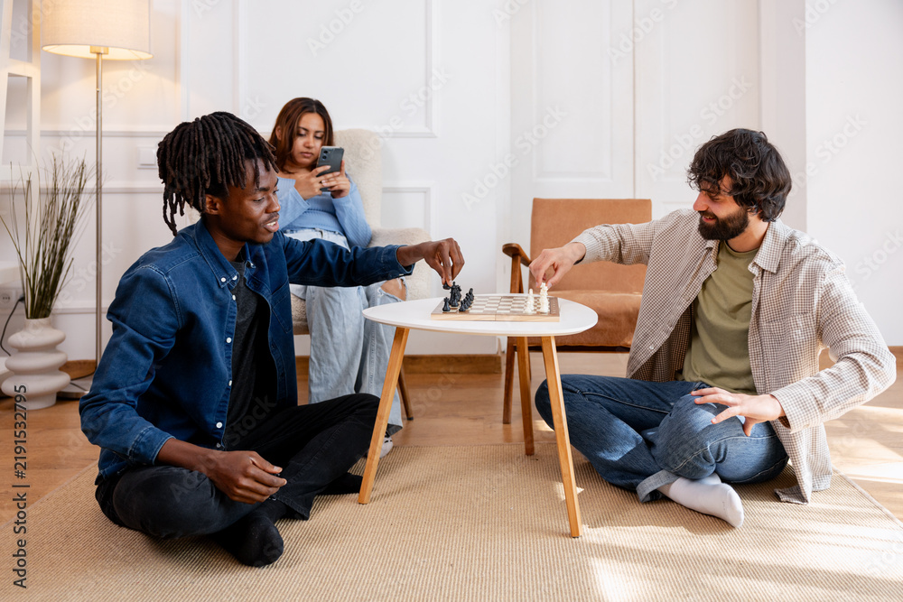 Fototapeta premium Diverse friends playing chess on floor enjoying leisure time