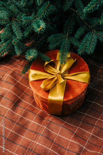 Christmas gift box with bow beside fir branch on brown checkered tablecloth, side view