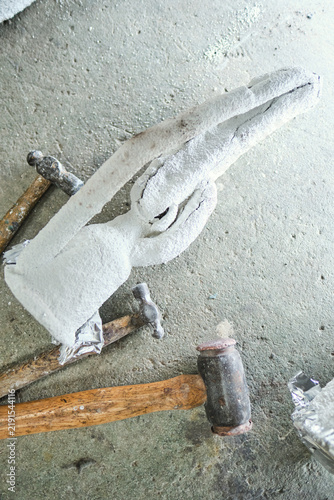 Фотография Newly cast metal sculpture remains encased in a cracked white plaster investment mould beside hammers during the lost wax casting process