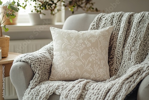 Jacquard damask cushion on grey armchair draped in heavy woolen blanket. Ideal for textile manufacturing promo banner, luxury home staging agency brochure or apartment rental website header