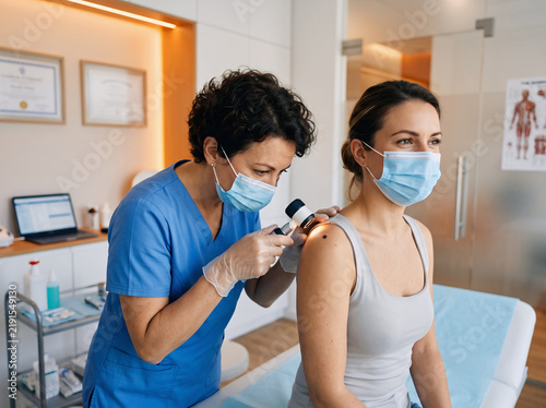 Dermatologist examining patient mole with dermatoscope skin cancer screening test in clinic