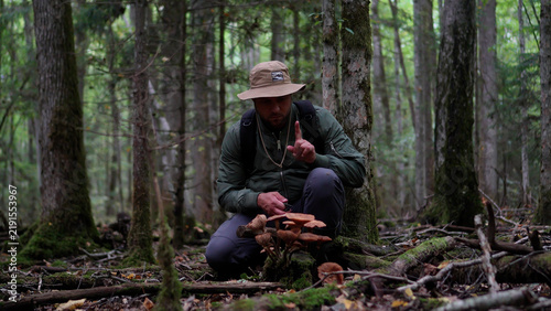 Foto Front view of a man showing a warning gesture while examining toxic wild mushrooms in an autumn forest