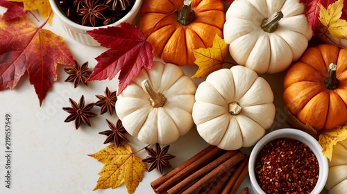 a flat lay composition features various pumpkins, autumn leaves, and spices. The pumpkins are white and orange, while the leaves are red, yellow, and green. The spices include star anise.