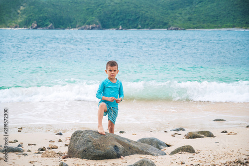boy schoolchild is posing by the beach by the sea during a summer vacation at tropical resort.