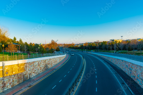 Street view in Samarkand, Uzbekistan, showing a broad divided roadway descending between landscaped park areas and stone retaining walls. Decorative railings, paved sidewalks, sparse traffic. 
