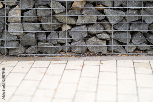 Canvastavla A robust gabion wall made of irregular grey stones contained by a sturdy metal w