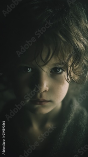Cinematic soft moonlight scene of a young child with messy hair and textured clothing looking at camera in foggy environment, dreamy poetic mood with cold tones and film grain