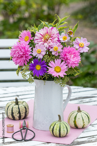 Blumenstrauß mit Sommerastern, Dahlie, Herbstanemonen, Efeu-Blüten und Weigelien-Blättern in einer Vase und Kürbisse im Garten 