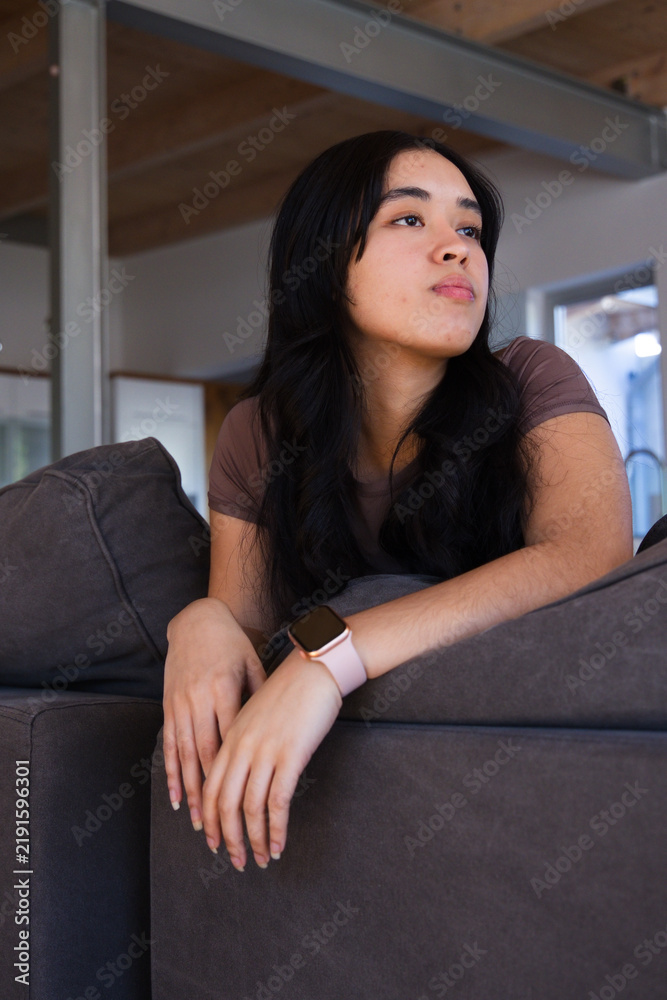 Obraz premium African American woman reclining on gray sectional couch in living room wearing pink smartwatch