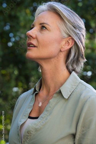 Bild auf Leinwand Senior woman looking upward in garden, wearing green button shirt, ribbed tank a