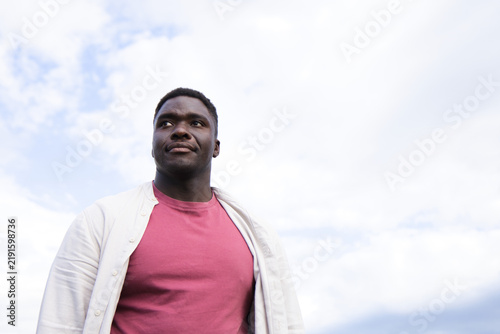 African American man standing gazing upward against sky wearing maroon tee and beige shirt