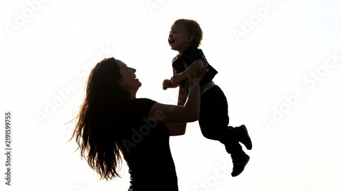 Silhouette of a happy mother lifting her small child into the air
