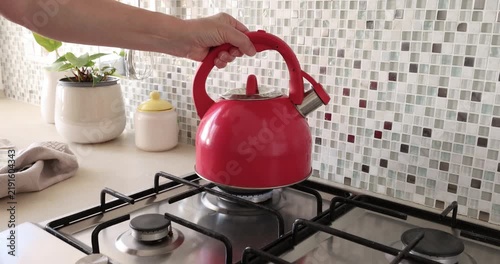 Placing red kettle on gas stove. Vintage home cooker kitchen appliances. Cozy morning routine cooking lifestyle.