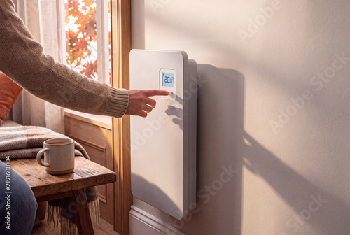 Personne réglant un radiateur électrique moderne avec thermostat numérique dans un intérieur chaleureux en automne, concept de confort thermique et d’économie d’énergie
