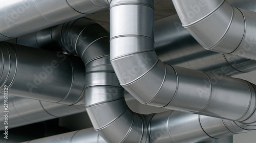 Industrial ventilation system featuring numerous galvanized metal air ducts and pipelines crisscrossing a ceiling, providing heating and cooling infrastructure to a building