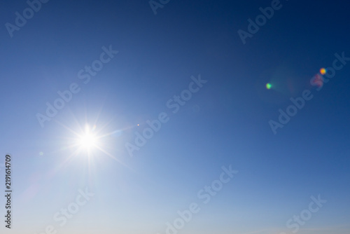 Bild auf Leinwand Bright midday sun shines in a clear blue sky, sending radiant sunlight rays and