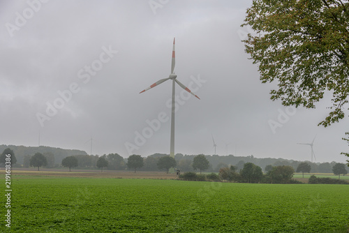 Tall wind turbine standing in a green field on a foggy overcast day in the countryside
