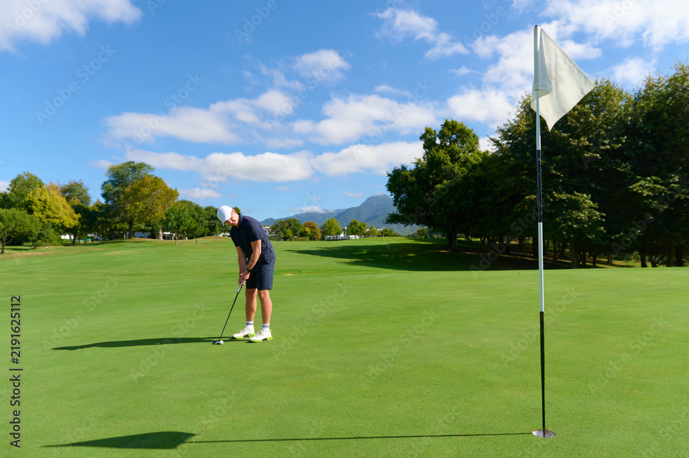 Obraz premium Man putting golf ball on green course.