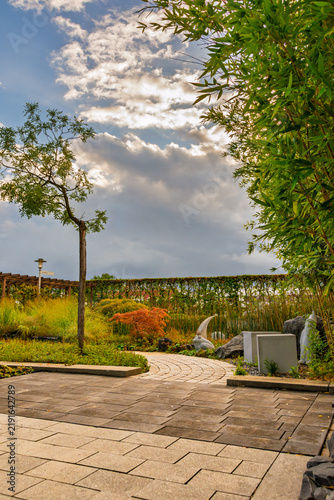 Paved path in a modern landscaped garden under a dramatic cloudy sky at sunset
