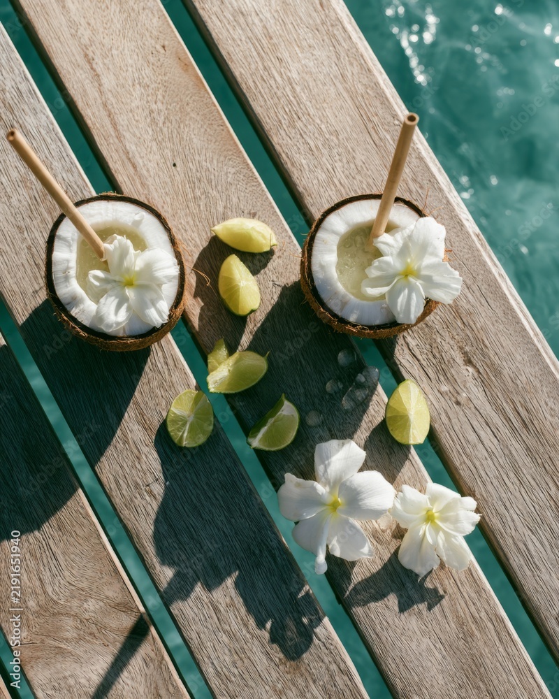Fototapeta premium Tropical coconut drinks with flowers on wooden pier above blue ocean