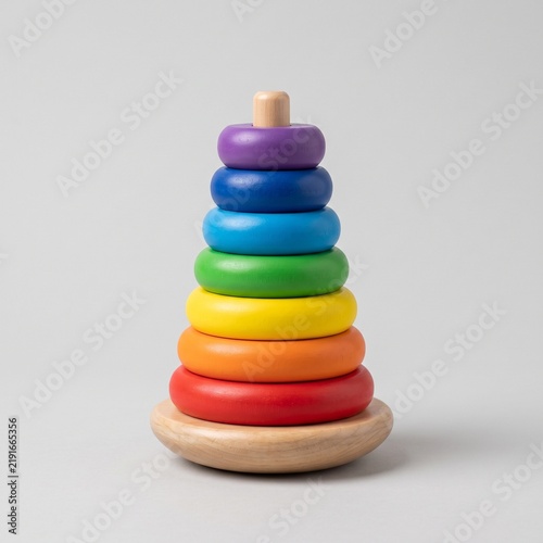 A colorful stacking ring toy with multiple bright rings arranged on a wooden base, isolated on a neutral background, representing early childhood development and educational play.