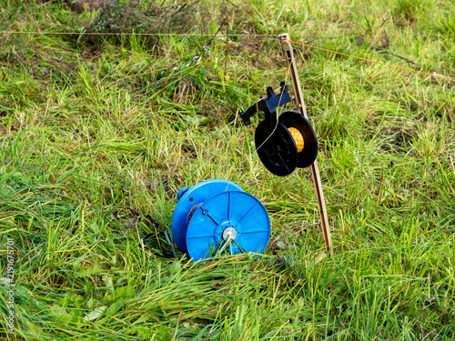 Konstfotografi Electric fence energizer and reel with orange wire installed in a green pasture,