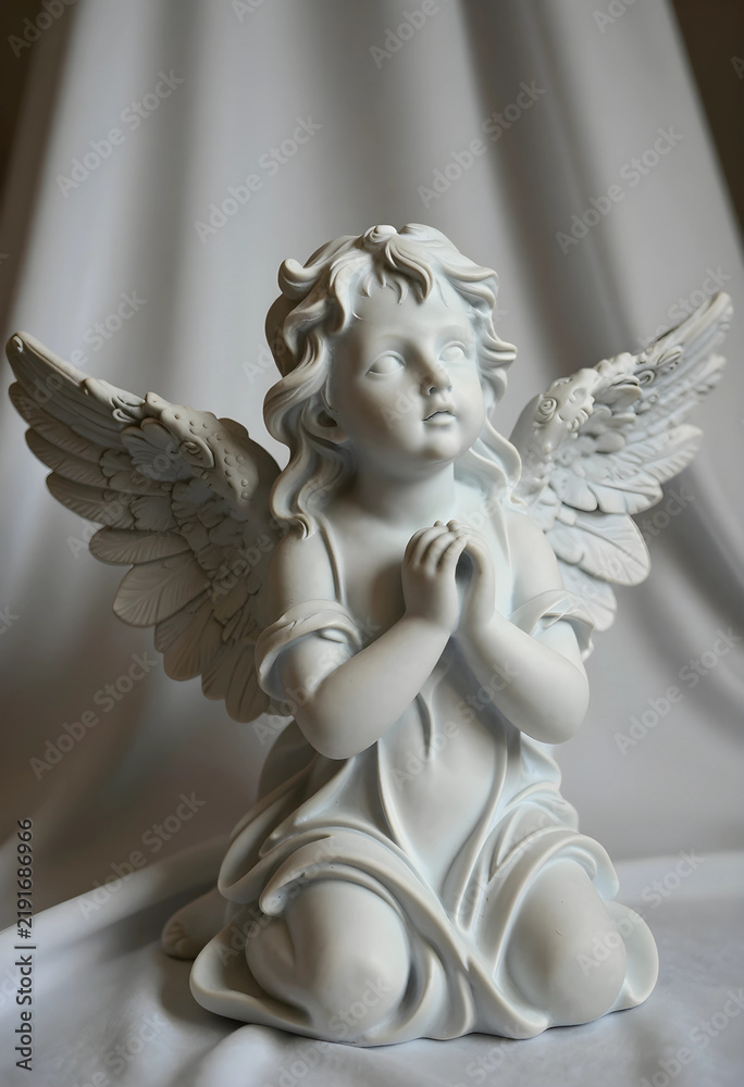 Fototapeta premium Spirituality and faith concept small angel statue with praying hands for religious peace hope and divine protection in a serene memorial setting