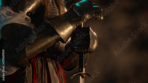 Unknown knight in steel armor resting armored hands on sword hilt. Footage suited for historical documentaries, fantasy video game marketing and cinematic storytelling