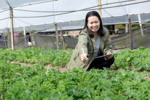 A young female farm owner uses a digital tablet to monitor and record crop growth on an organic vegetable farm.