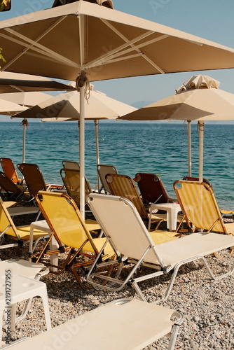 Fotografía Beach chairs and umbrellas on a pebbled shore, photographic style, sea backgroun