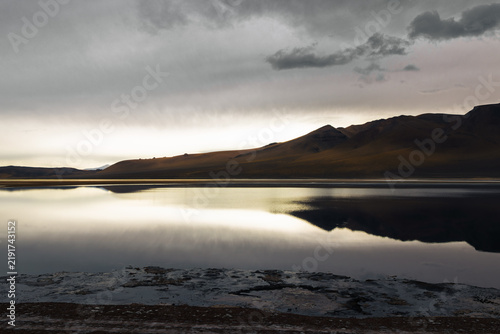 Fotografie Salar de tara’s mirror-like salt flat reflects golden mountains and a moody clou