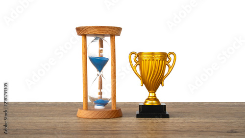Foto Golden trophy cup standing beside hourglass with blue sand on wooden table isola