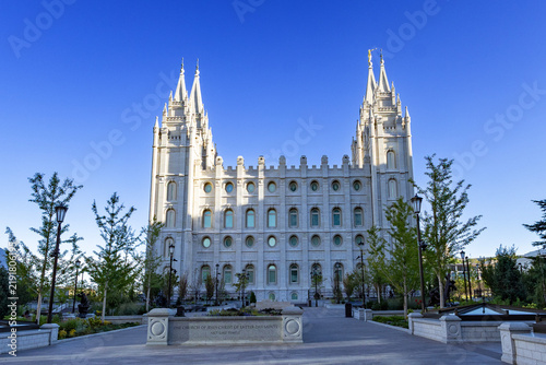 Salt Lake City Utah Temple and surrounding grounds with beautifully landscaped gardens, trees, pathways, and historic architecture. A peaceful summer scene showcasing the iconic temple and its grounds