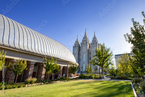 Salt Lake City Utah Temple and surrounding grounds with beautifully landscaped gardens, trees, pathways, and historic architecture. A peaceful summer scene showcasing the iconic temple and its grounds