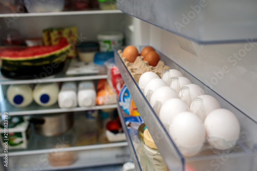 Fresh eggs stored in open refrigerator door tray, white and brown eggs neatly arranged closeup, eggs kept cold inside refrigerator shelf compartment, high quality photo