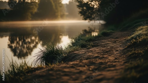 Misty riverbank path at sunrise with golden light.