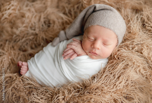Newborn baby swaddled in white sleeping on fuzzy fur.. Newborn photo session