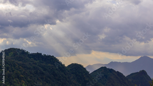 Sunbeams break through heavy storm clouds, illuminating the forested mountains of Sri Lanka's central highlands near Maskeliya.