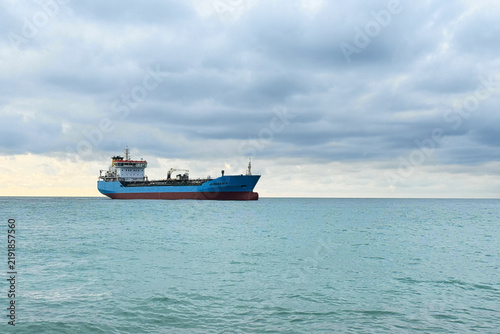 A large ship sails on the water in the ocean. The sky is filled with clouds, showing different shades of gray