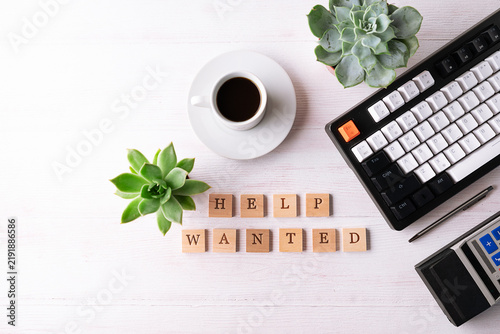Office desktop with keyboard, succulent flowers, cup of coffee and text Help Wanted on the wooden cubes. Hiring and recruitment of staff concept.
