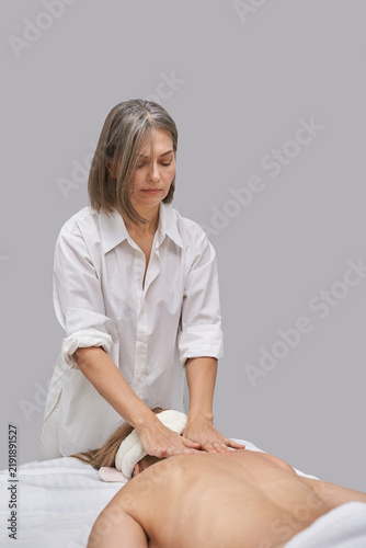 Foto Female Massage Therapist Working On Upper Back Of Supine Woman In Quiet Spa Room With Neutral Backdrop And Soft Lighting