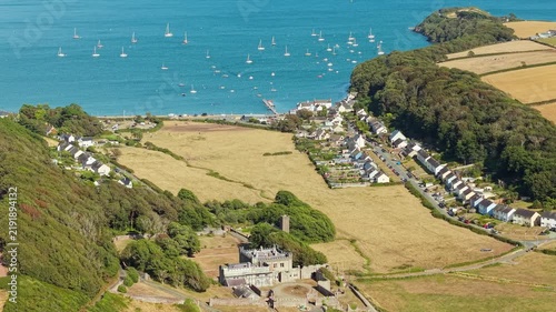Aerial view of Dale village and castle grounds in Pembrokeshire, yellow fields leading down to calm waters dotted with moored sailboats