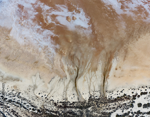 Aerial view of intricate sediment drainage patterns and salt deposits on a desert landscape with sparse scrubby vegetation in Australia.
